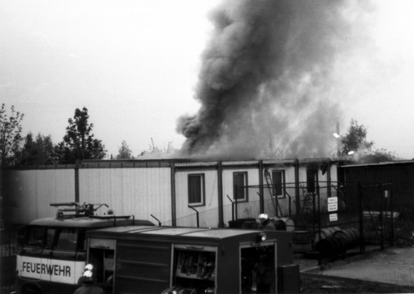 Einsatzfahrzeug vor rauchender Baracke