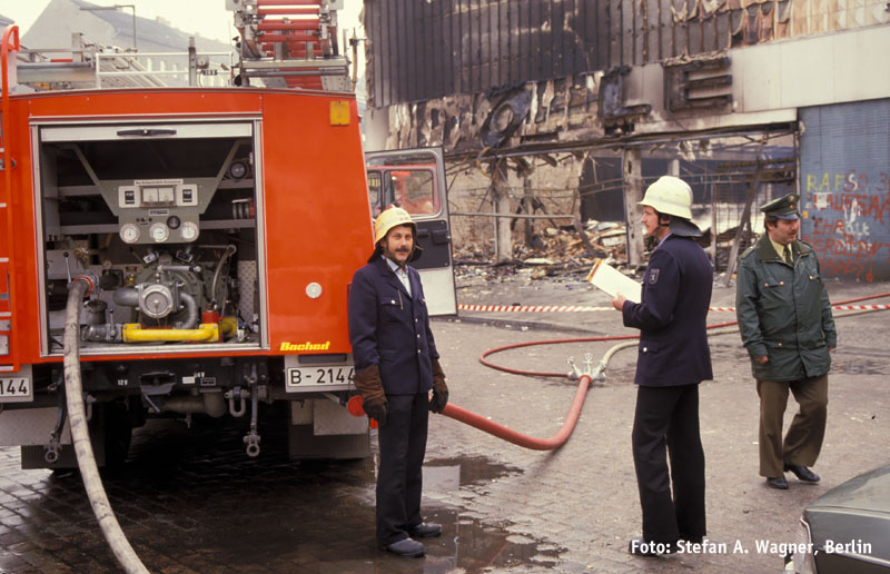 Löschfahrzeug mit Feuerwehrleuten vor Brandruine