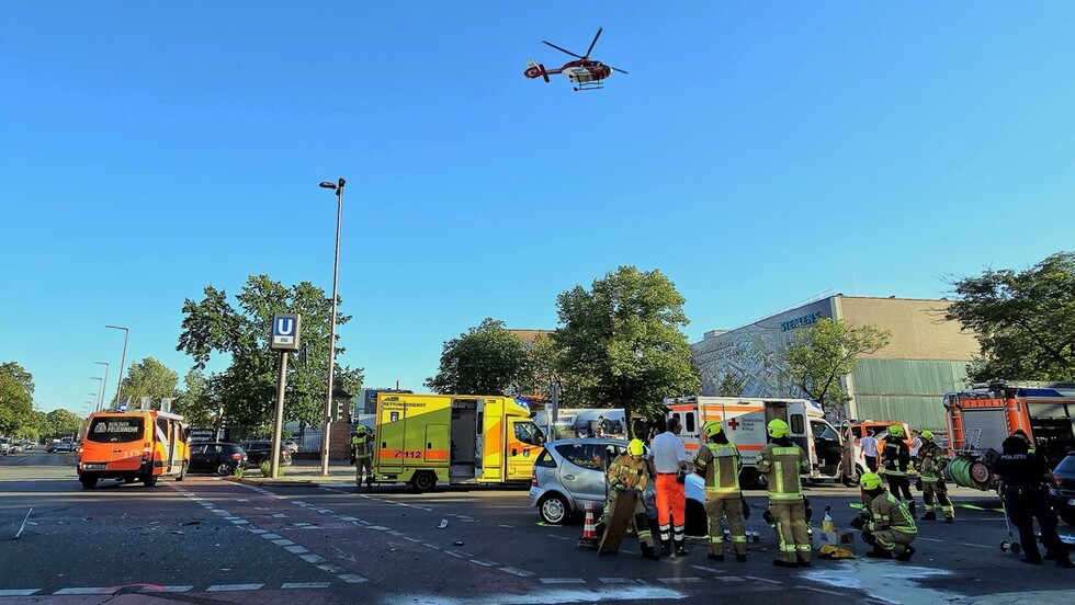 Einsatzkräfte bei der Bergung eines der verunfallten Fahrzeuge mit startenden Rettungshubschrauber im Hintergrund.