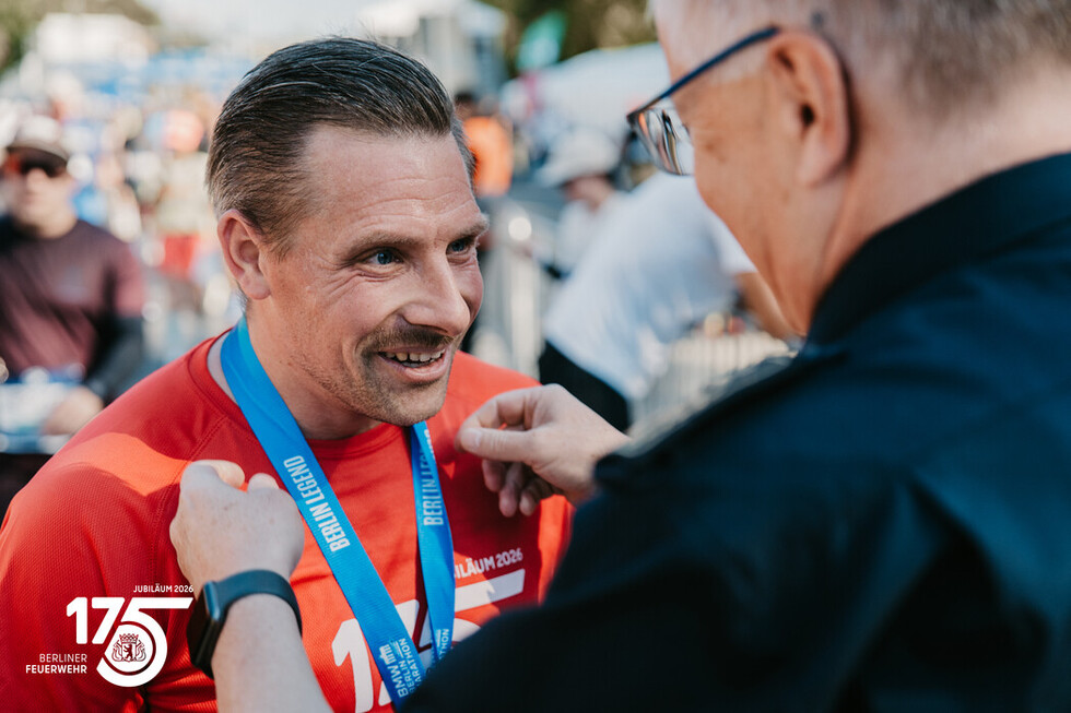 Landesbranddirektor Prof. Dr. Karsten Homrighausen überreicht einem Angehörigen der Berliner Feuerwehr nach dem Zieleinlauf die Finisher-Medaille.