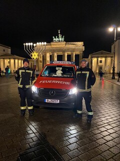 Zwei Einsatzkräfte der Freiwilligen Feuerwehr neben einem Einsatzfahrzeug vor dem nächtlichen Brandenburger Tor