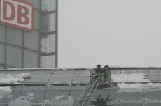 Zwei Feuerwehrleute im Korb einer Drehleiter entfernen Eis vom Dach des Hauptbahnhofs