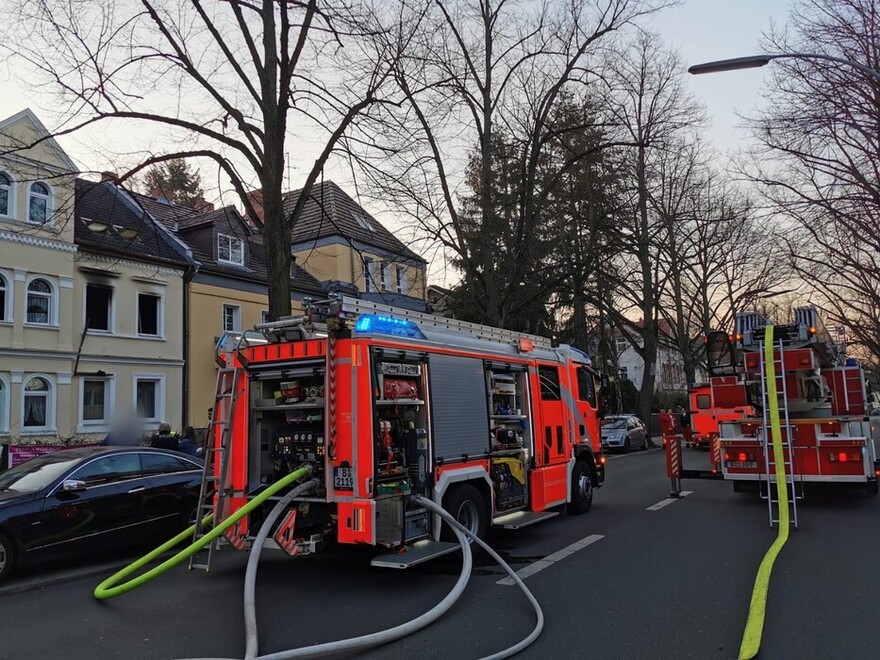 Löschfahrzeug vor dem betroffenen Gebäude. Schläuche gehen vom Fahrzeug ab und führen zum Brandobjekt.