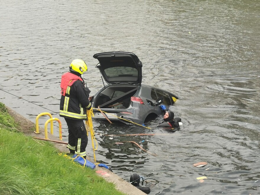 Feuerwehrmann steht am Ufer und gibt den im Wasser befindlichen Taucher Anweisungen.