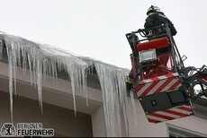 Feuerwehrmann im Korb einer Drehleiter beim Entfernen von Eisapfen an einer Dachkante 
