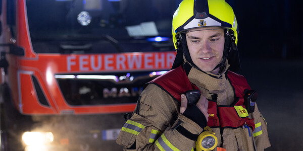 Feuerwehrmann mit Helm vor Einsatzfahrzeug