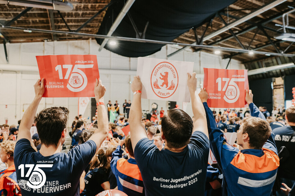 Mitglieder der Jugendfeuerwehr halten Schilder zum 175‑jährigen Jubiläum der Berliner Feuerwehr hoch.