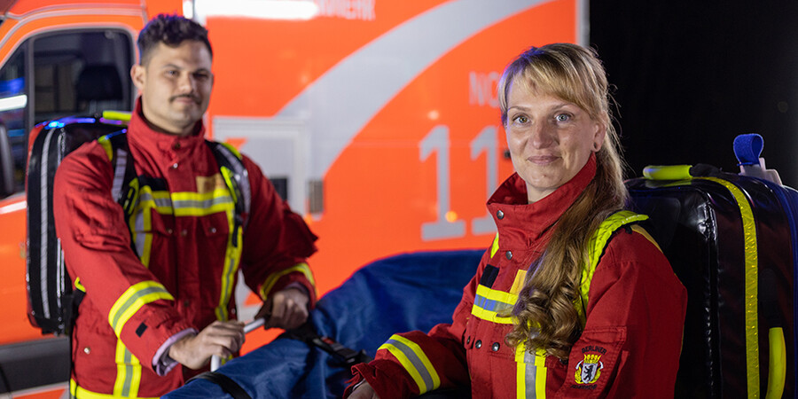 Mann und Frau in Rettungsdienstkleidung vor Einsatzfahrzeug