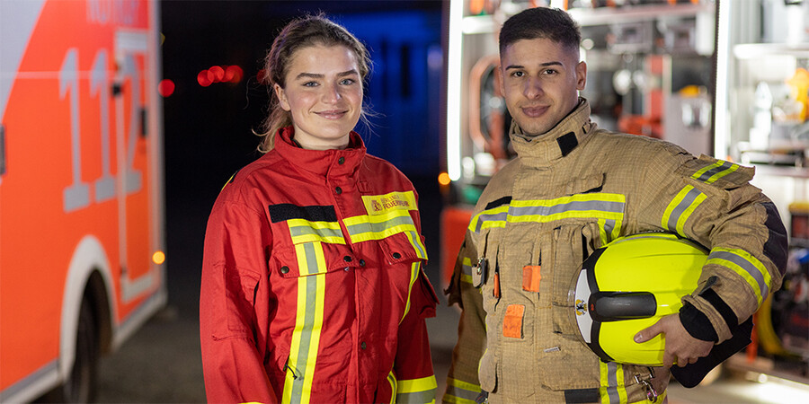 Frau in Rettungsdienstkleidung, Mann in feuerwehrschutzkleidung mit Helm unter dem Arm