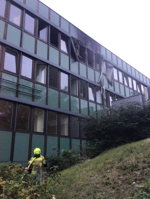 Feuerwehrmann schaut auf die vom Feuer beschädigte Fassade des Ärztehauses.