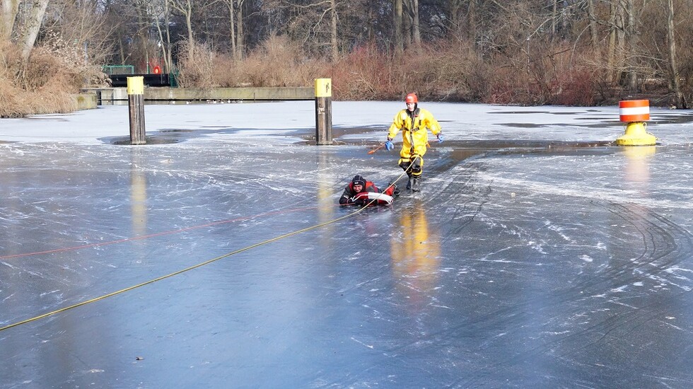 Rettung einer Person mittels Rettungsring durch einen Kollegen im Eisrettungsanzug.