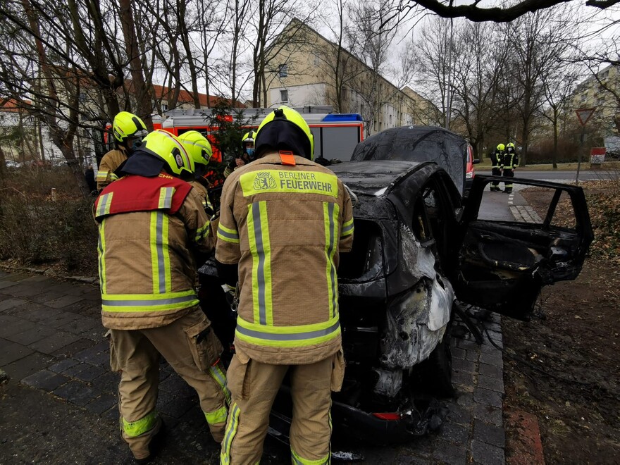 Einsatzkräfte kontrollieren den ausgebrannten Pkw.