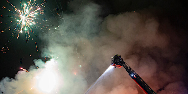Zwei Feuerwehrleute im Korb der Drehleiter, Nachthimmel mit Feuerwerk