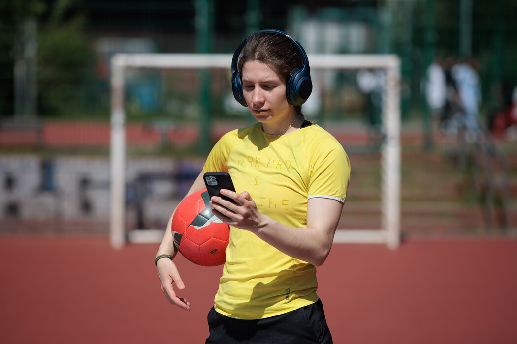 Frau mit Ball unter dem Arm blickt auf ein Smartphone