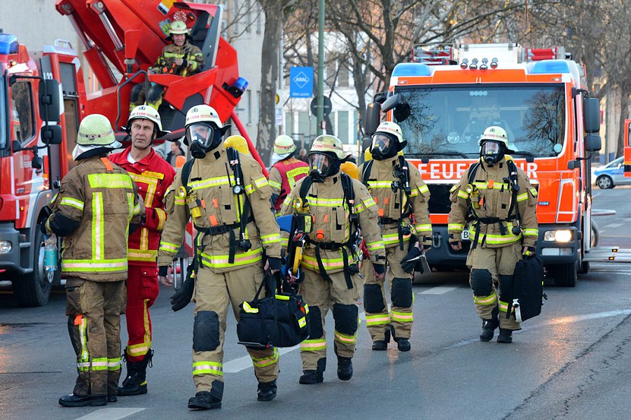 Gruppe von Feuerwehrleuten, hintereinander laufend, im Hintergrund Löschfahrzeuge