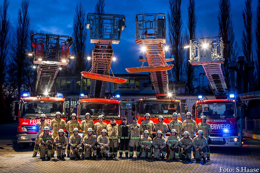 Gruppenfoto von Auszubildenden und Ausbildern. Im Hintergrund vier Drehleiterfahrzeuge.