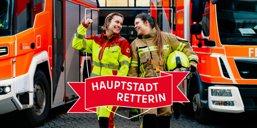 Zwei Frauen in Einsatzkleidung vor Feuerwehrfahrzeugen