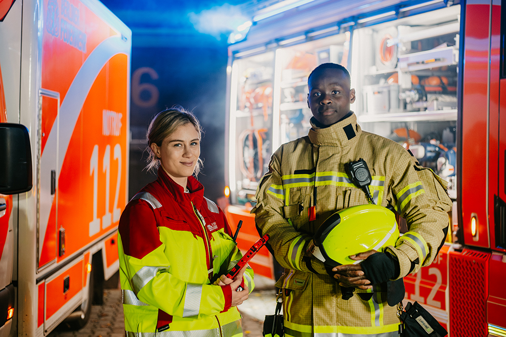 Notfallsanitäterin und Feuerwehrmann stehen vor Einsatzfahrzeugen