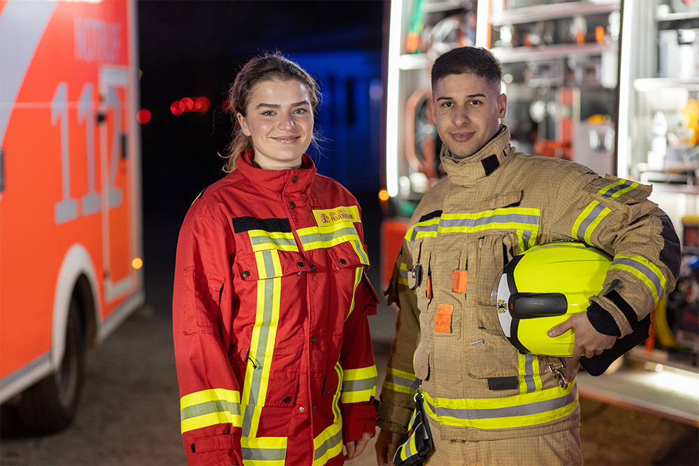 Frau in Rettungsdienstkleidung, Mann in Feuerwehrschutzkleidung